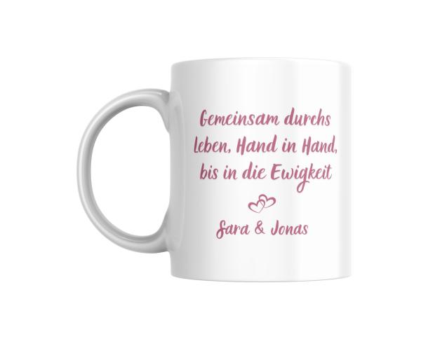 Weiße Tasse mit romantischem Spruch in rosaner Schrift: ‚Gemeinsam durchs Leben, Hand in Hand, bis in die Ewigkeit‘ und zwei ineinandergreifenden Herzen darunter, personalisiert mit den Namen ‚Sara & Jonas‘. Ein liebevolles Design, ideal als Geschenk für